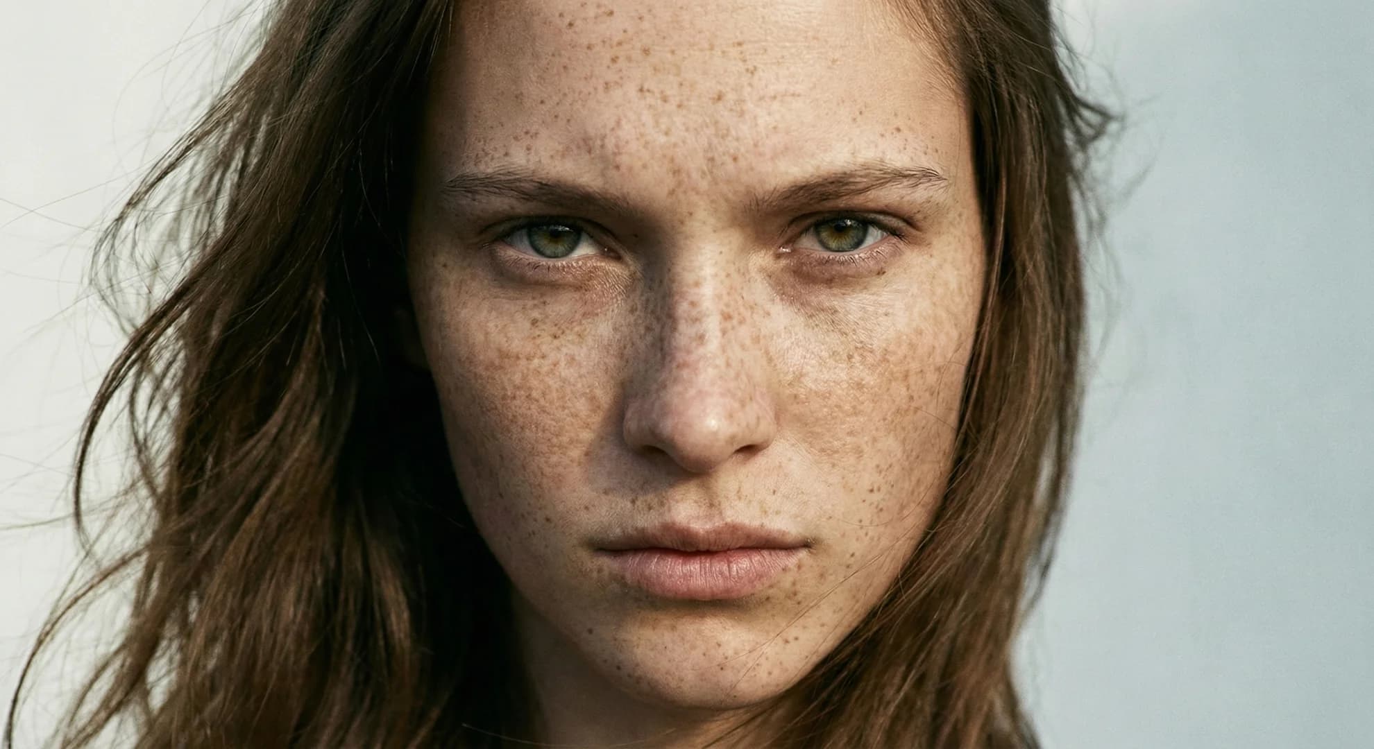 Close-up portrait of a woman with green eyes and prominent freckles across her face.